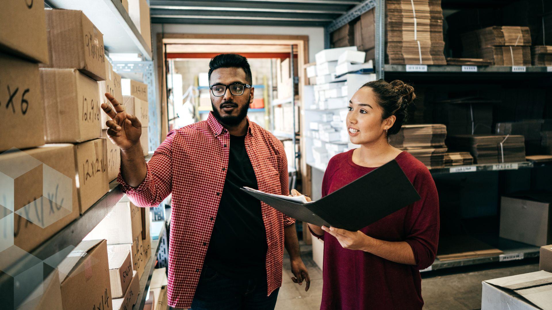 A man and a woman check boxes in a small warehouse
