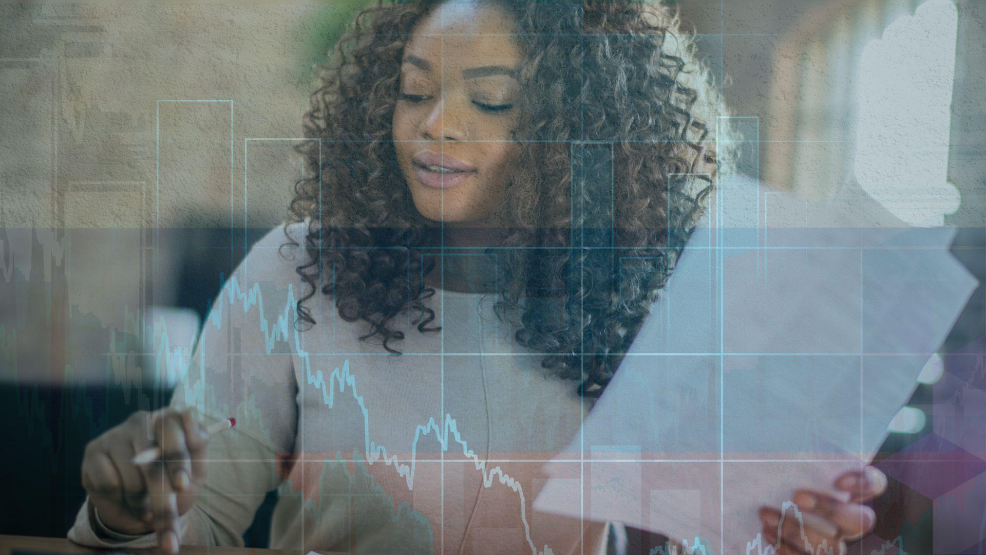 A woman with curly hair sits at a table adding up bills