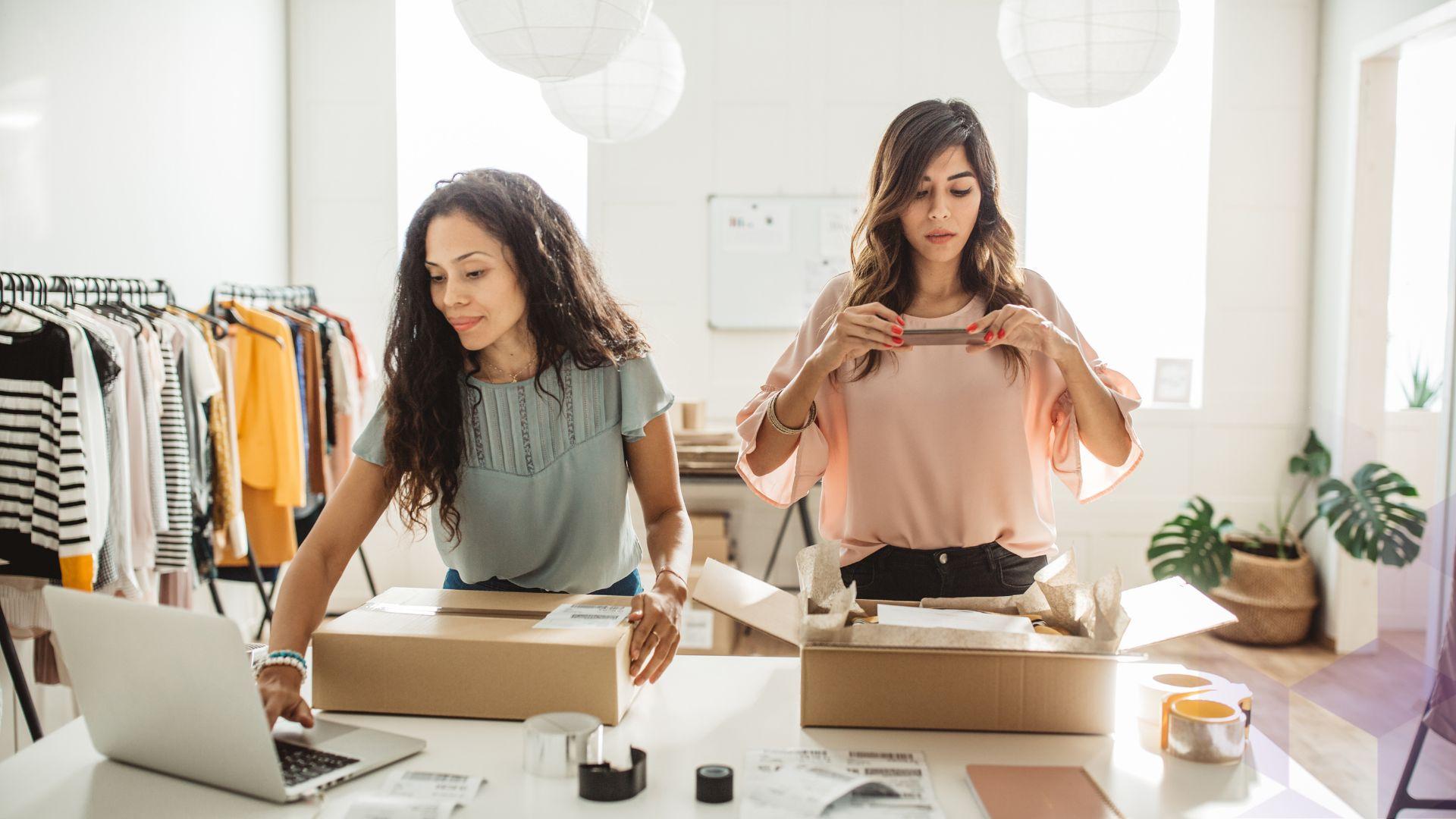 Two women work alongside each other, photographing and packing clothes