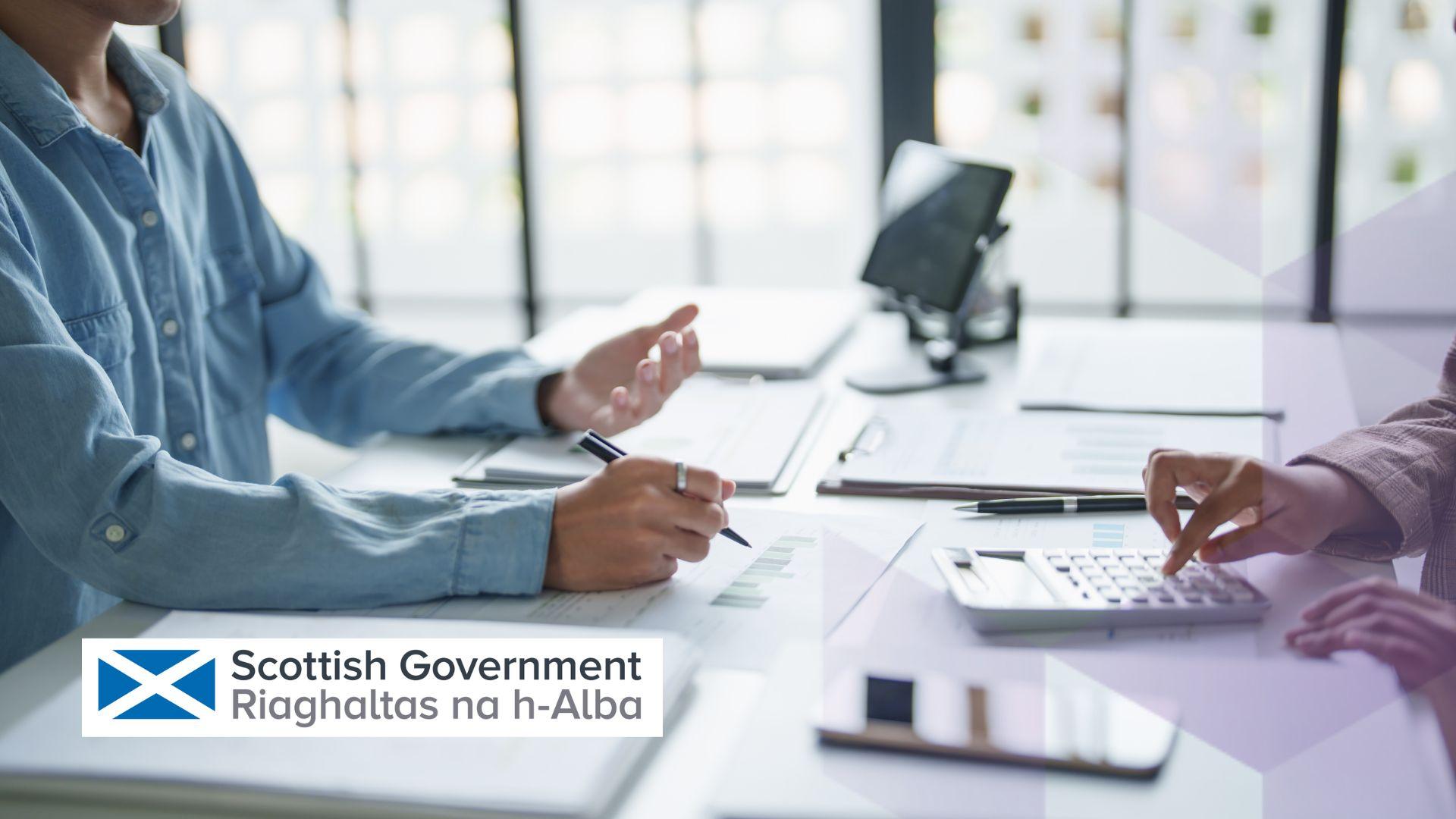 Two people sit across from each other at a desk discussing business