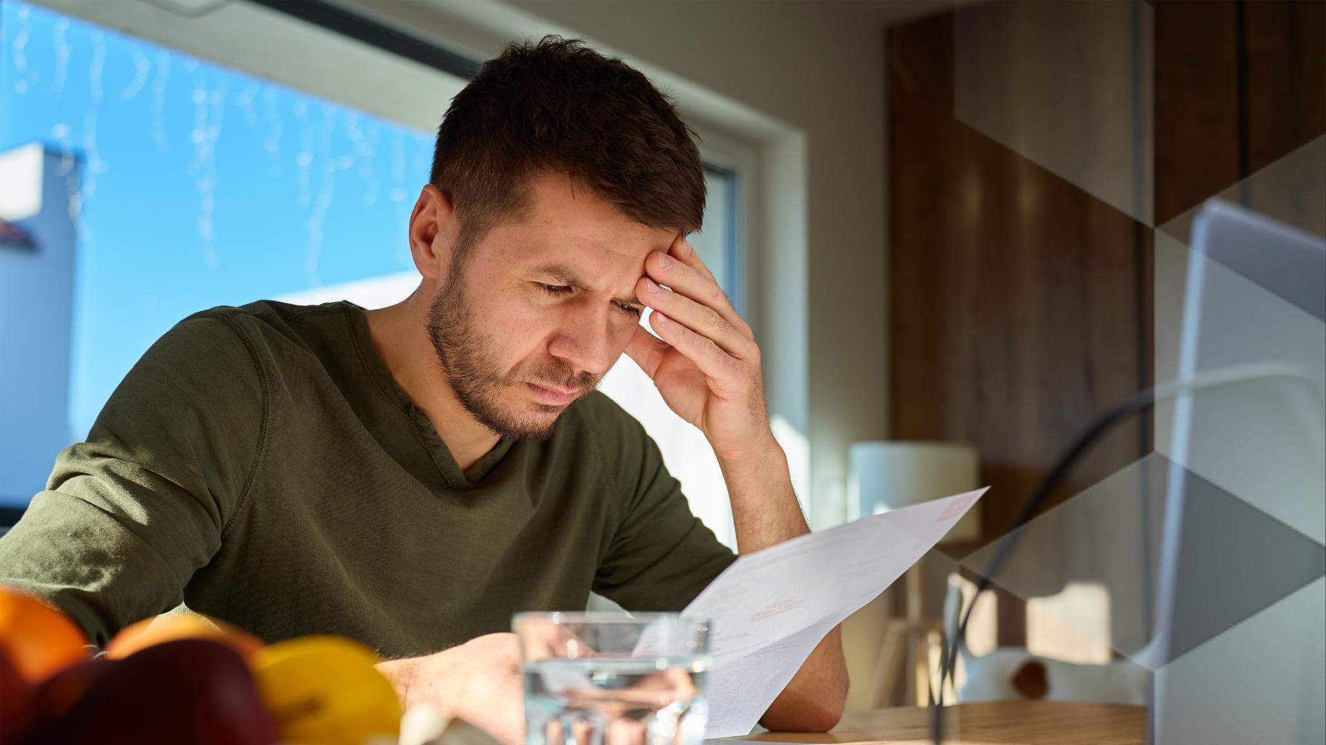 A worried looking man sits at a computer looking at a bill