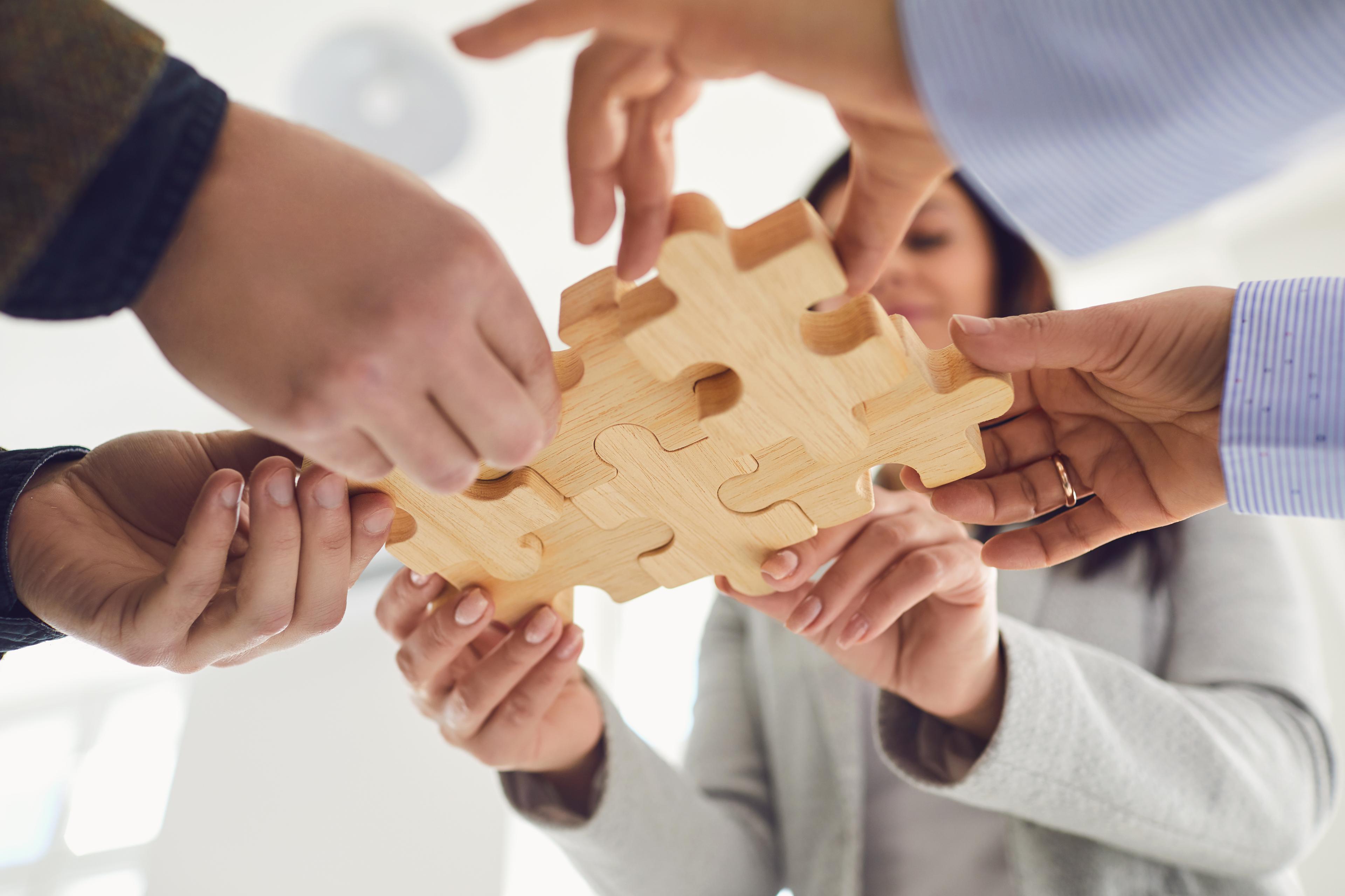 Hands bringing together wooden puzzle pieces